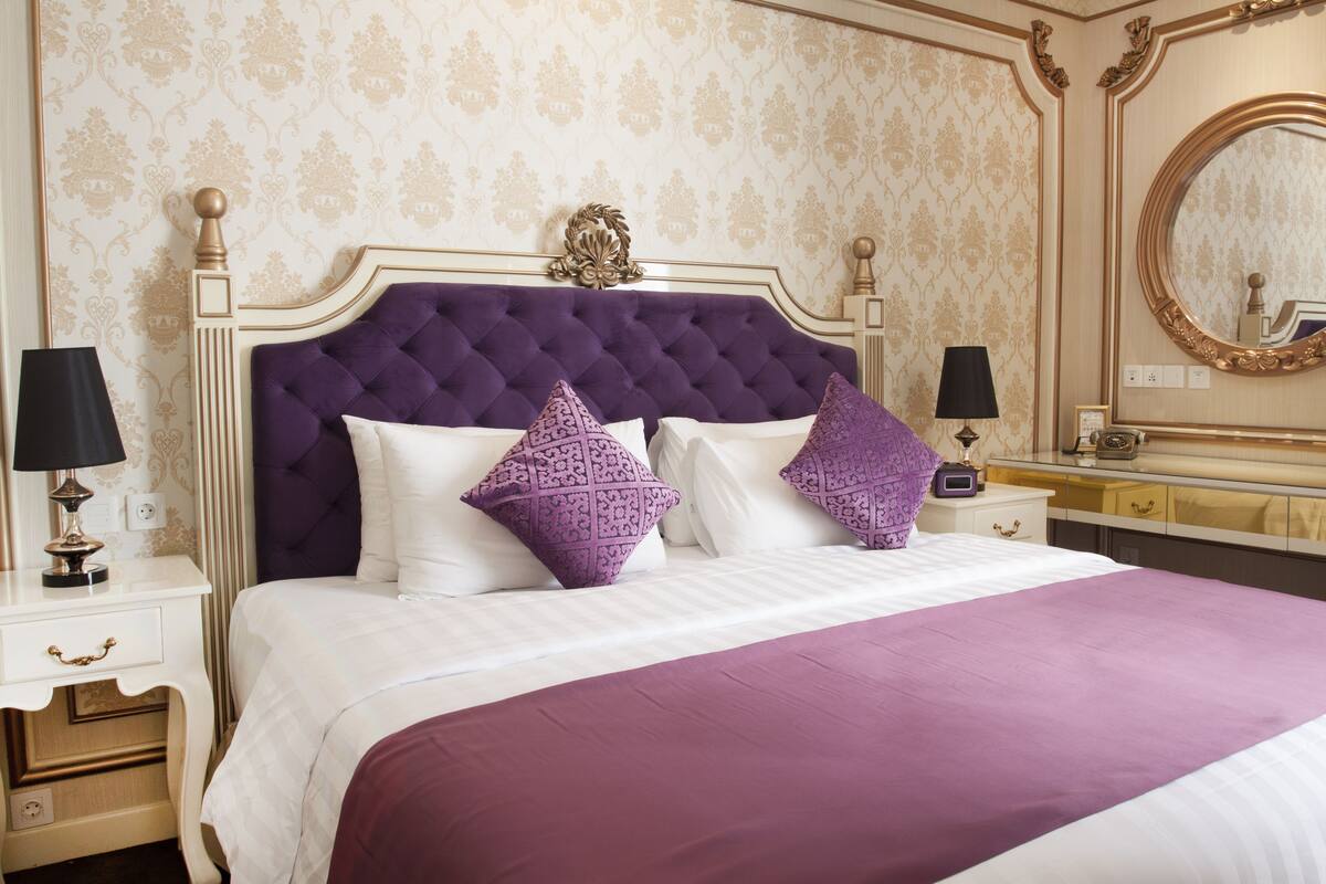 Ein luxuriöses Schlafzimmer mit einer gesteppten Kopfteil, weißer Bettwäsche und lilafarbenen Akzenten.