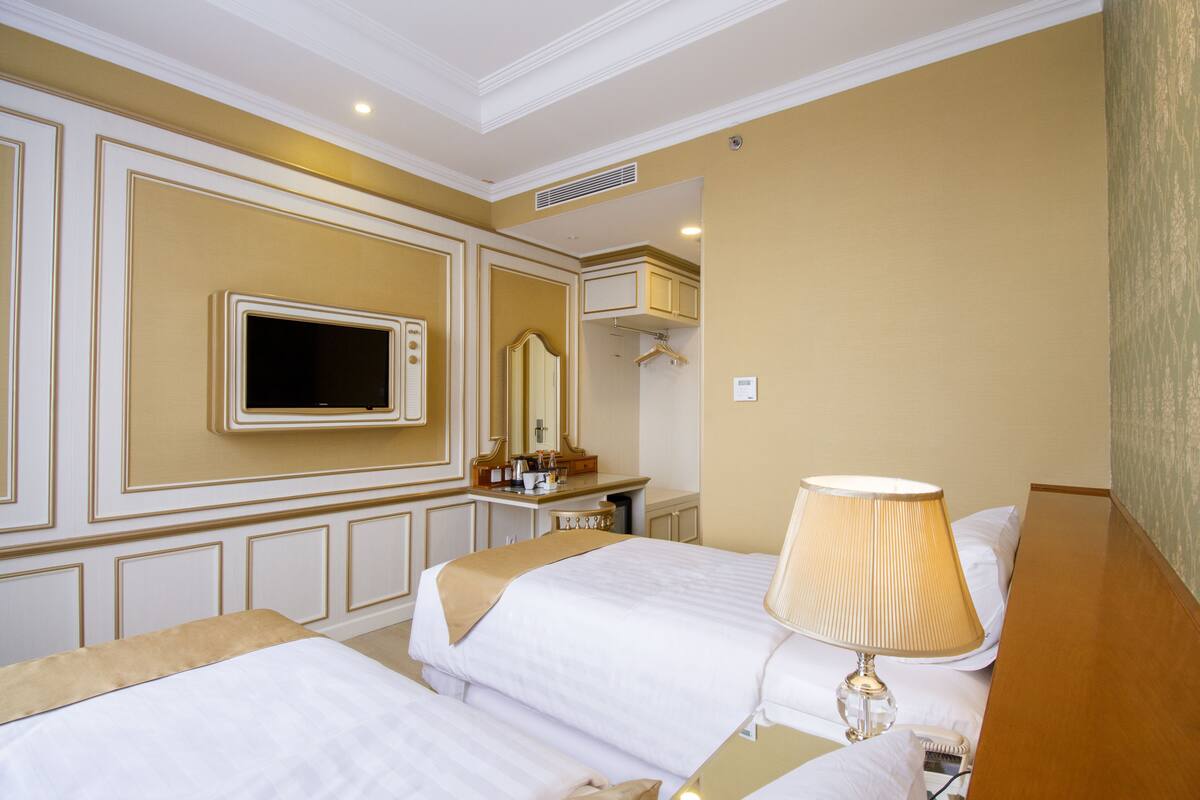 Ein Hotelzimmer mit zwei Betten, einem Fernseher, einem Spiegel, einem Schreibtisch und einer Lampe.