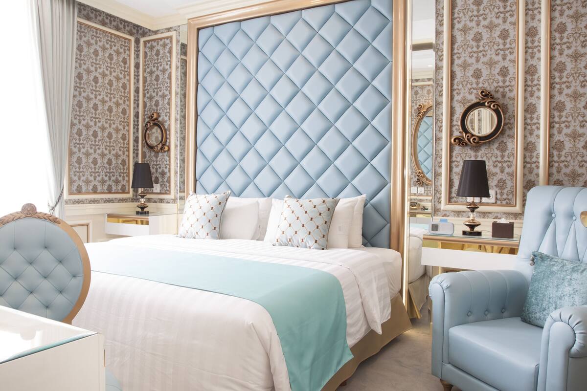 Ein geräumiges Schlafzimmer mit einem großen Bett, einem gepolsterten Kopfteil, einer Sitzecke mit einem Sessel und einem Nachttisch mit einer Lampe.