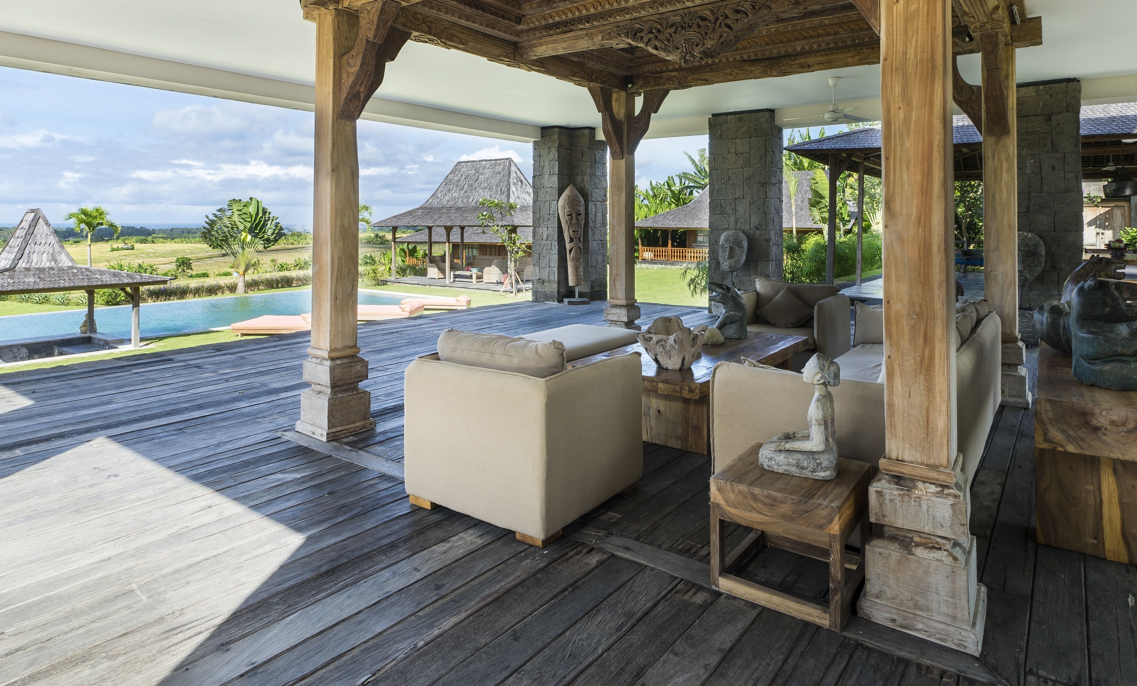 A wooden deck with outdoor seating, a stone pillar, and a view of a pool and landscape.