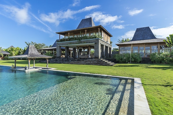 A large house with a swimming pool, a covered patio, and a well-maintained lawn.
