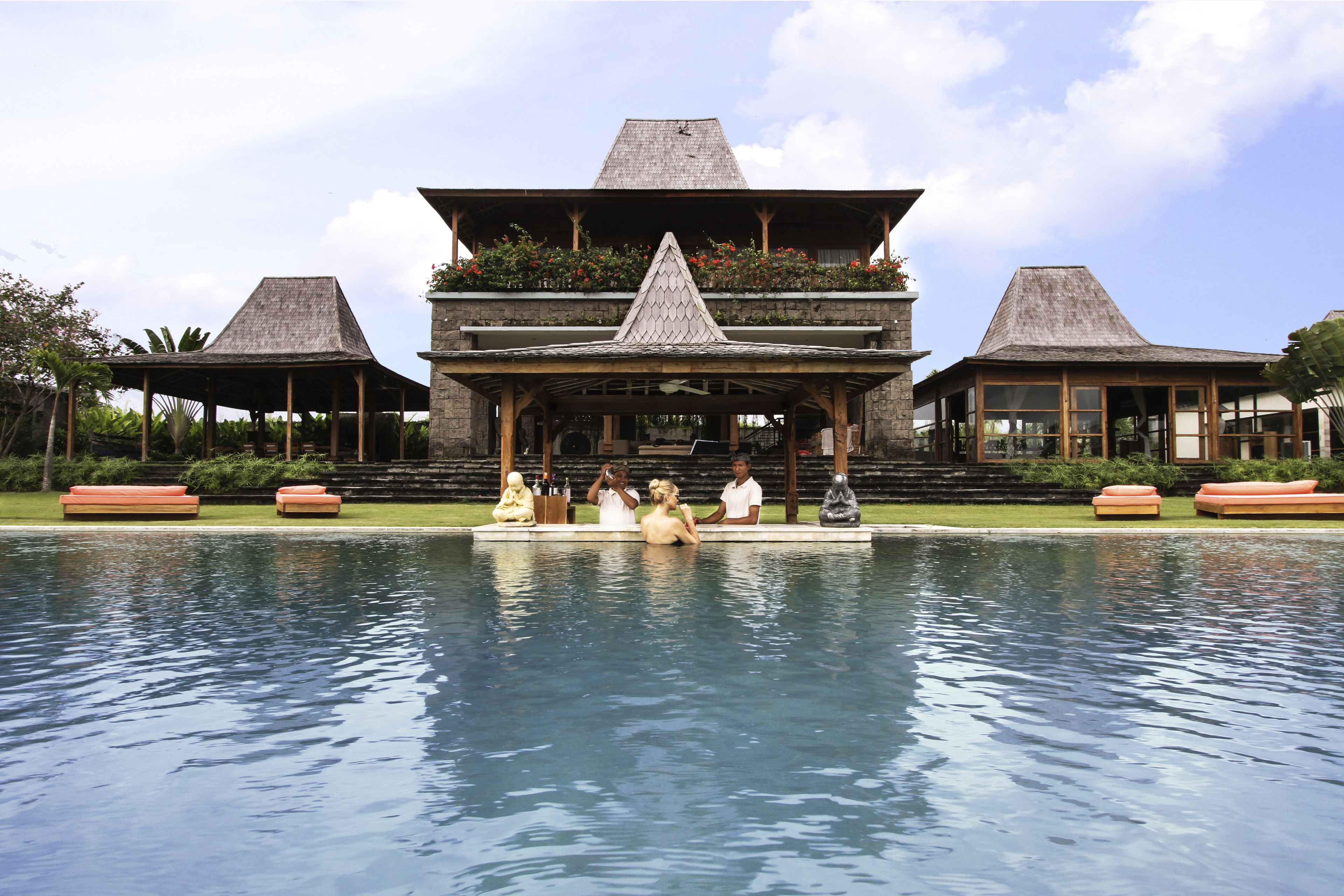 A resort with a large pool, a covered seating area, and a building with a unique architectural design.