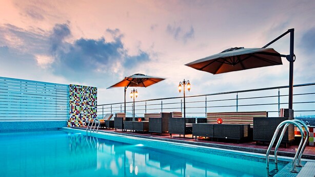 Un área de piscina en la azotea con sillones, sombrillas y un muro de azulejos.