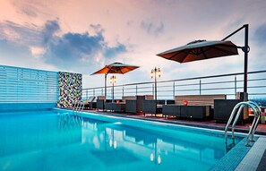 A rooftop pool area with lounge chairs, umbrellas, and a tiled wall.