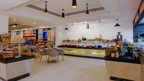 Una cafetería moderna con un mostrador central, zona de estar y diversas exhibiciones de comida y bebidas.