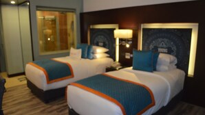Habitación de hotel con dos camas, cada una con cubrecama azul y naranja, una mesita de noche con lámpara y un espejo grande en la pared.