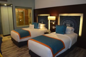 A hotel room with two beds, each with a blue and orange bedspread, a nightstand with a lamp, and a large mirror on the wall. - Zone by the Park ORR Chennai (Chennai)