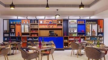 Un restaurante moderno con varias mesas y sillas, una barra azul y distintos productos alimenticios y bebidas en estantes.