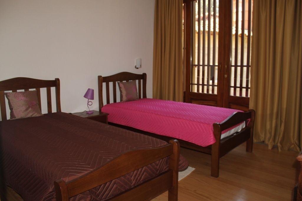 A bedroom with two wooden beds, a nightstand with a lamp, and a window with curtains.