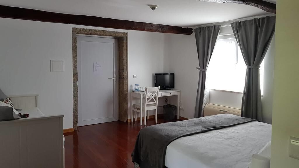 A hotel room with a bed, a desk with a chair, a television, and a window with curtains.
