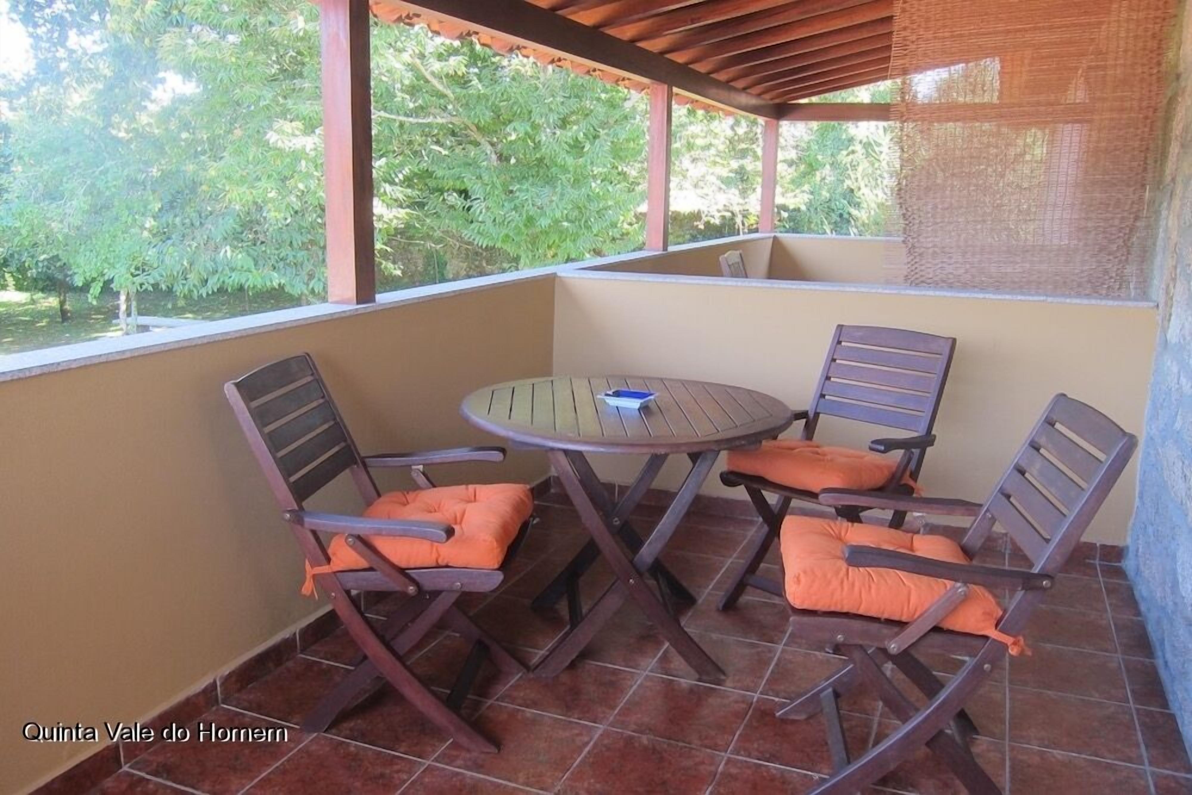 A covered patio with a round table and four chairs, each with orange cushions.