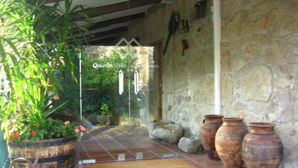 A stone wall entrance with a glass door, potted plants, and terracotta pots. - Quinta Vale do Homem (Amares)