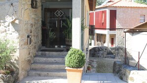 A stone building with a glass entrance, steps leading up to it, and a potted plant in front. - Quinta Vale do Homem (Amares)