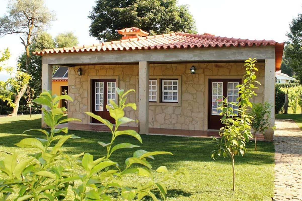 A small, single-story building with a tiled roof and stone walls, surrounded by a well-maintained lawn and trees.
