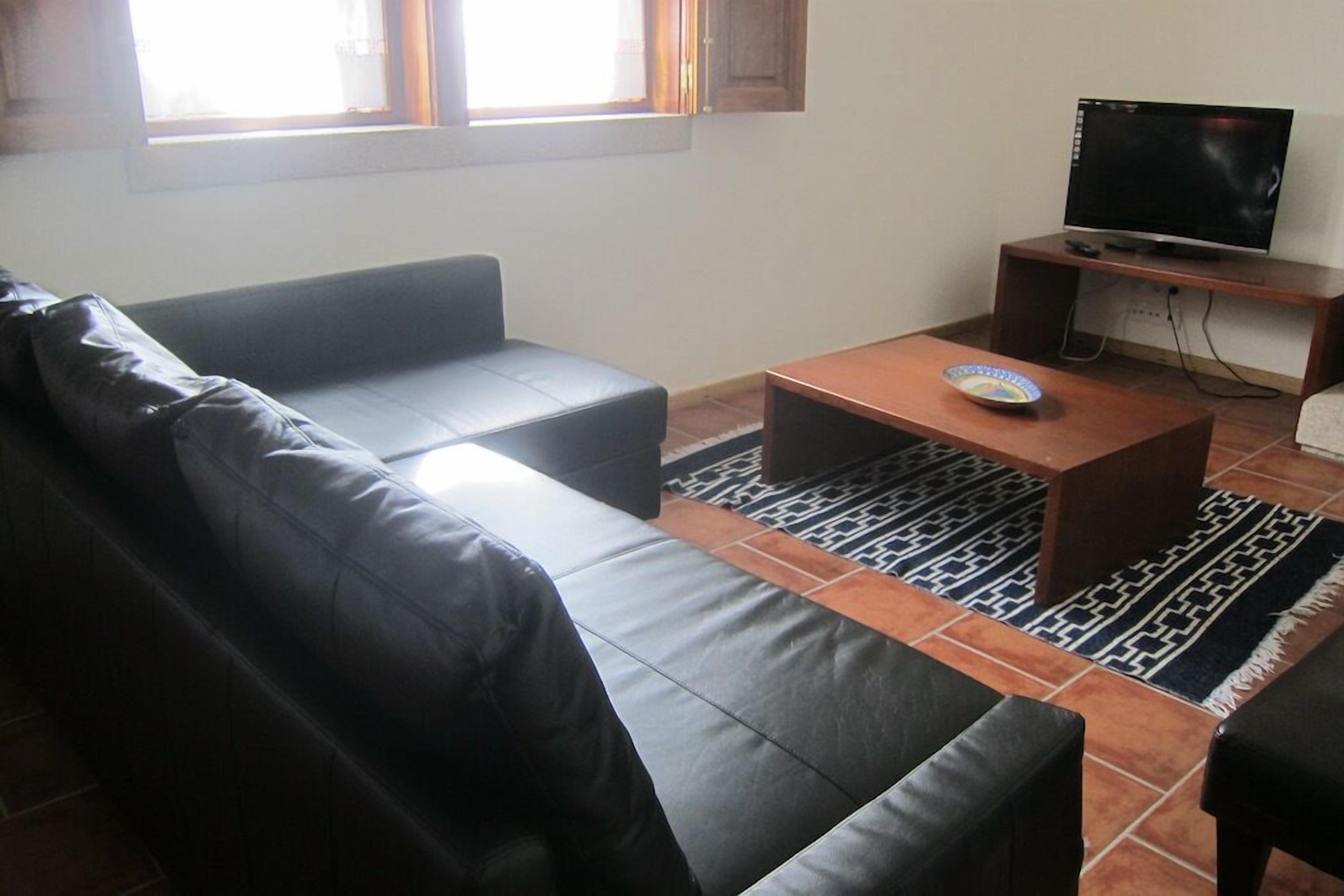 Una sala de estar con un sofá de cuero negro, una mesa de centro de madera y un televisor sobre un mueble de madera.