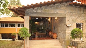 A stone building with a tiled roof, a wooden door, and steps leading to a porch. There are potted plants on the porch and a sign above the door. - Quinta Vale do Homem (Amares)