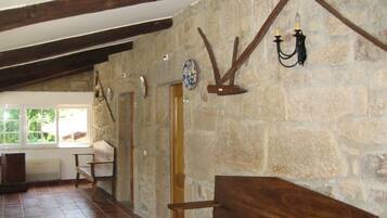 Una habitación rústica con paredes de piedra, vigas de madera, un banco y una araña.