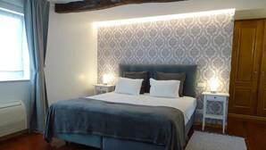 A bedroom with a bed, two bedside tables, a nightstand, a window with curtains, and a patterned wallpaper. - Quinta Vale do Homem (Amares)