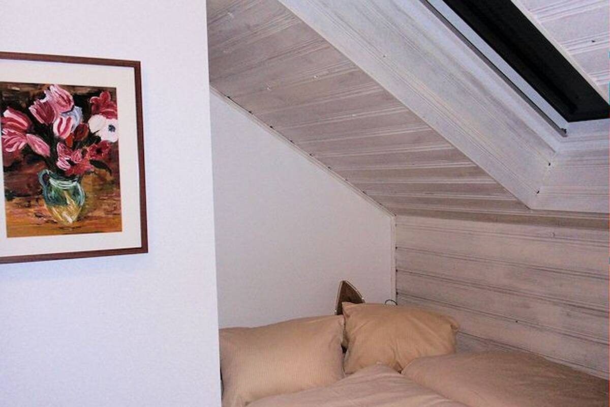 A bedroom with a sloped ceiling, a bed with beige bedding, and a framed painting of flowers on the wall.
