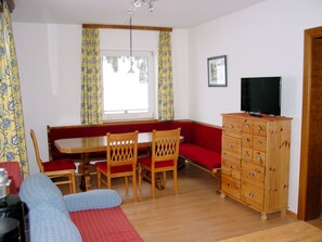 A room with a wooden cabinet, a television, a sofa, and a dining table with chairs.
