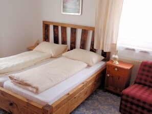 A double wooden bed with white bedding, a nightstand with a lamp, and a plaid chair.