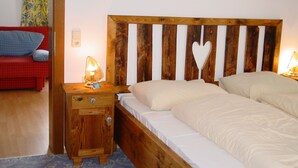 A bedroom with a wooden headboard, a bedside table with a lamp, and a red couch in the corner.