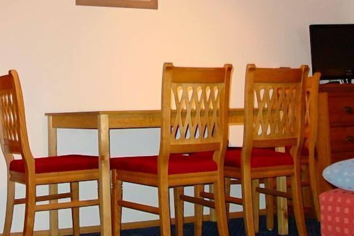 A room with a wooden table and four chairs, a television, and a bed with a patterned bedspread.