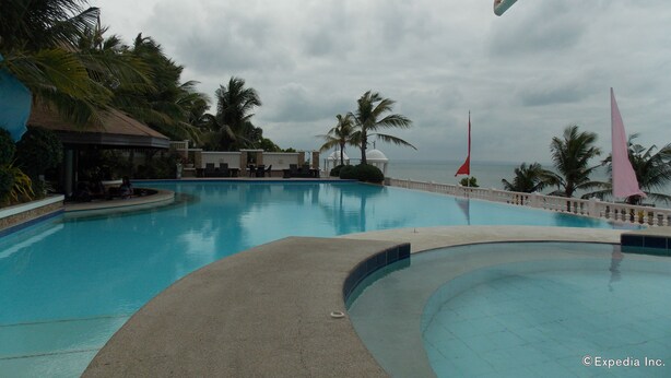 A swimming pool with lounge chairs and palm trees, surrounded by a white fence and a view of the ocean. - Bearland Paradise Resort (Tigbauan)