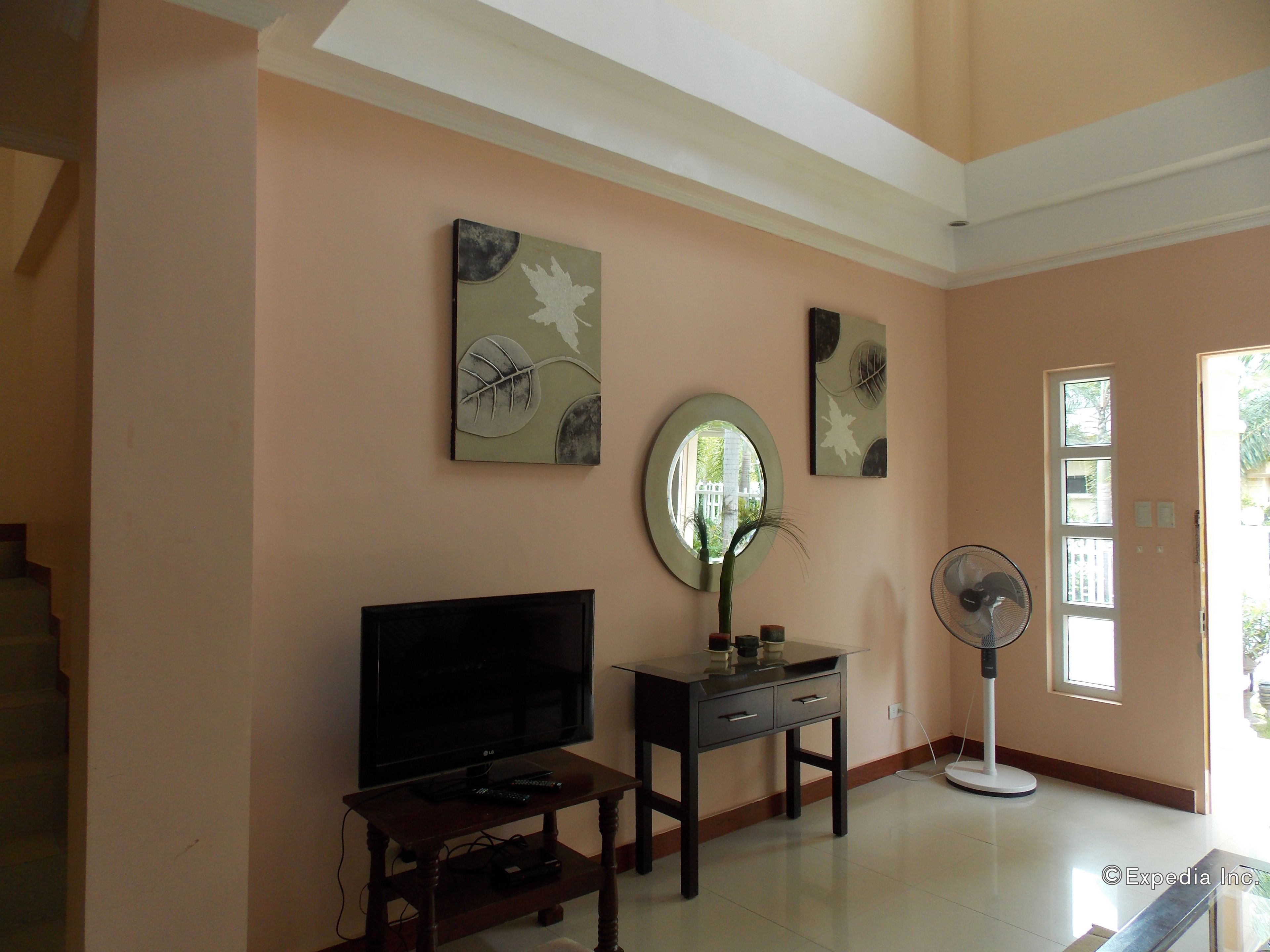 A living room with a flat-screen TV, a small table, a decorative mirror, and a standing fan.