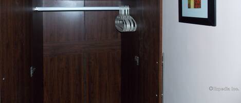 Un armario de madera con barra metálica y ganchos, y dos cuadros enmarcados en la pared.