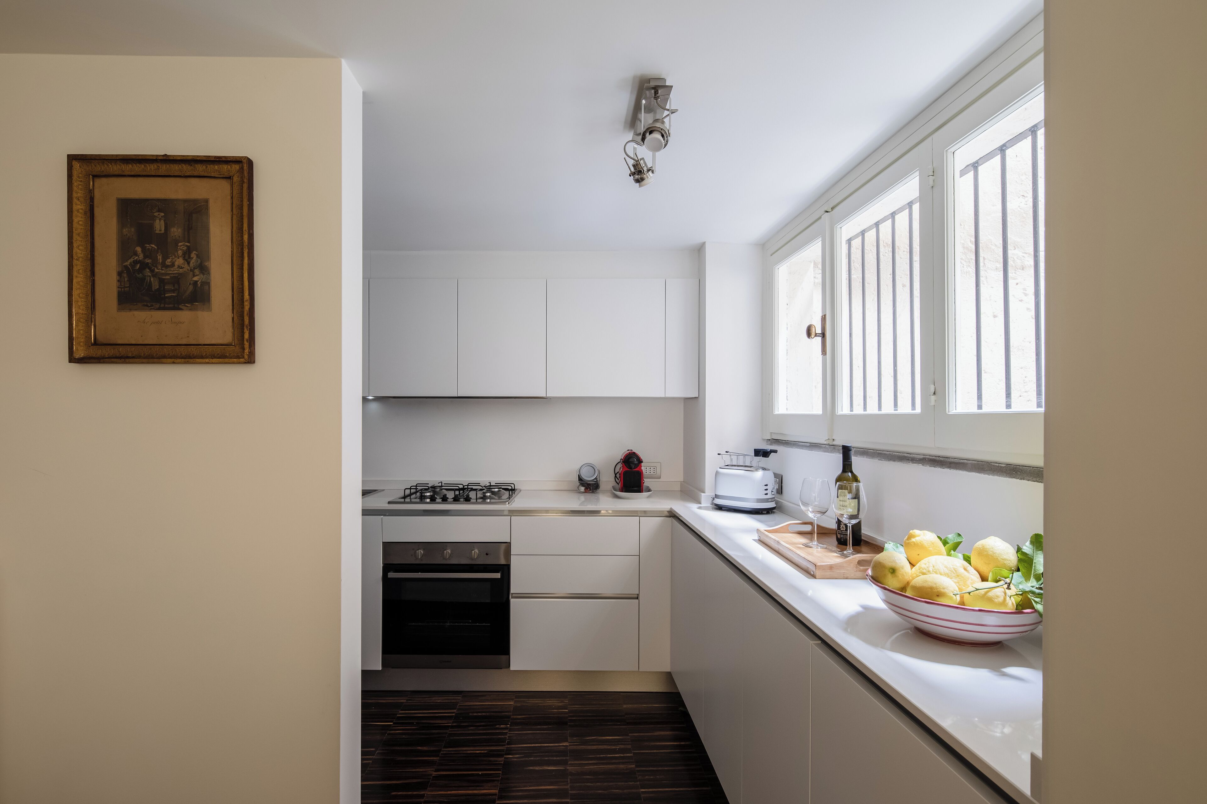 A compact kitchen with white cabinets, a gas stove, a toaster, and a bowl of lemons on the counter.