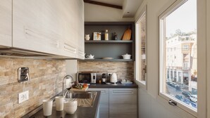 A modern kitchen with a stone backsplash, stainless steel appliances, and a view of the street through a large window. - Your Suite Rome (Rome)
