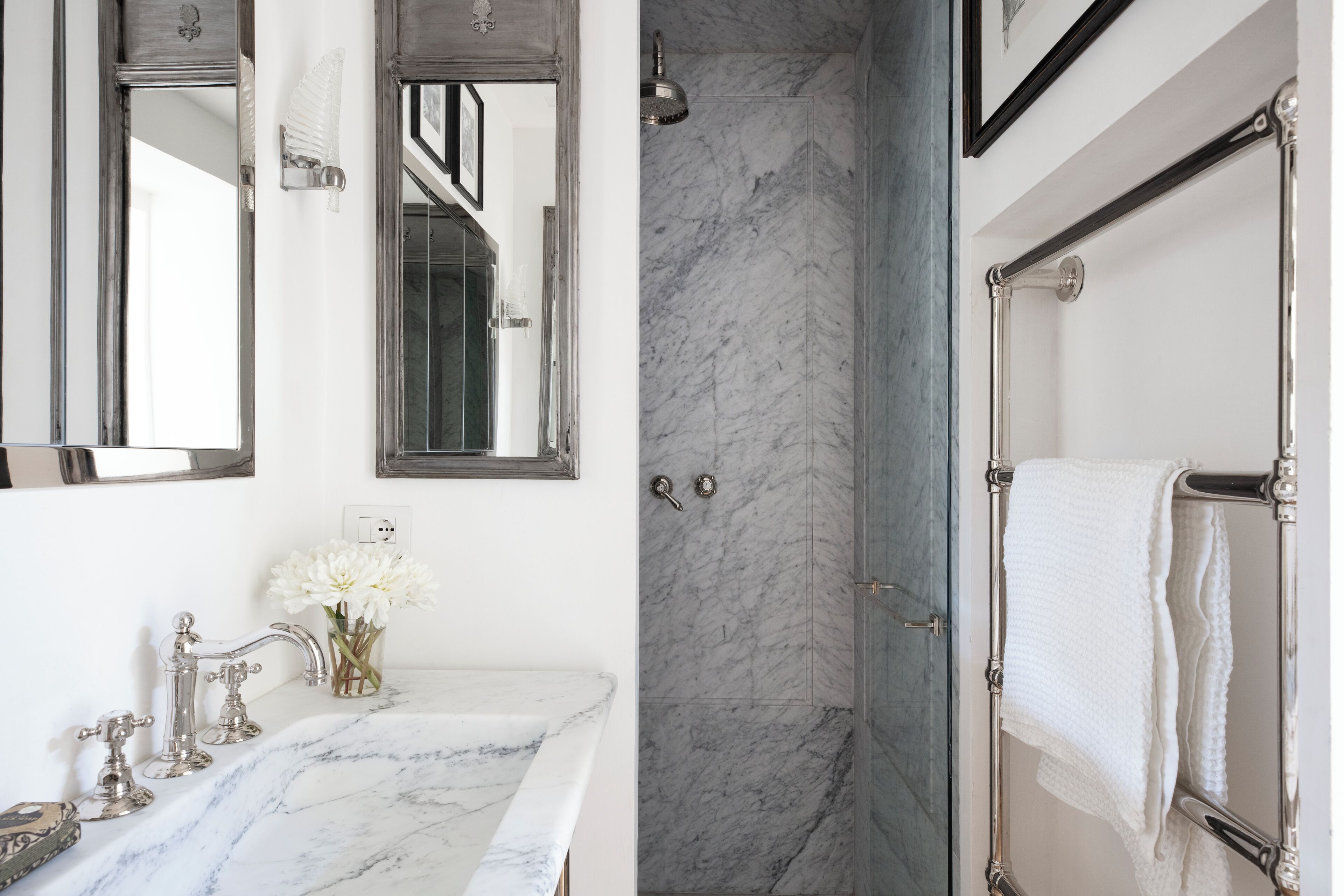 A bathroom with a marble sink, a glass shower enclosure, and a towel rack.