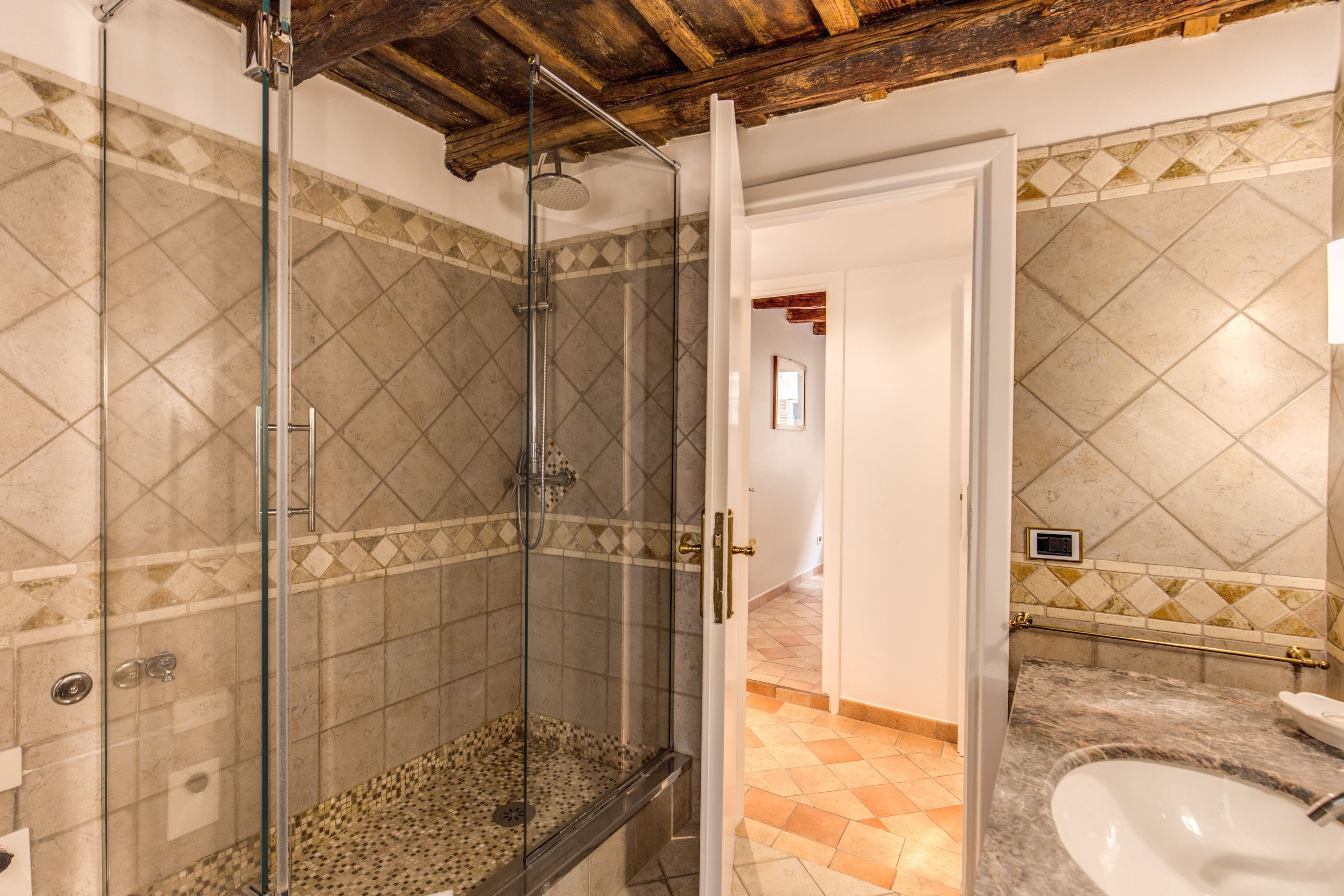 Un baño con ducha de vidrio, lavamanos y piso de azulejos.
