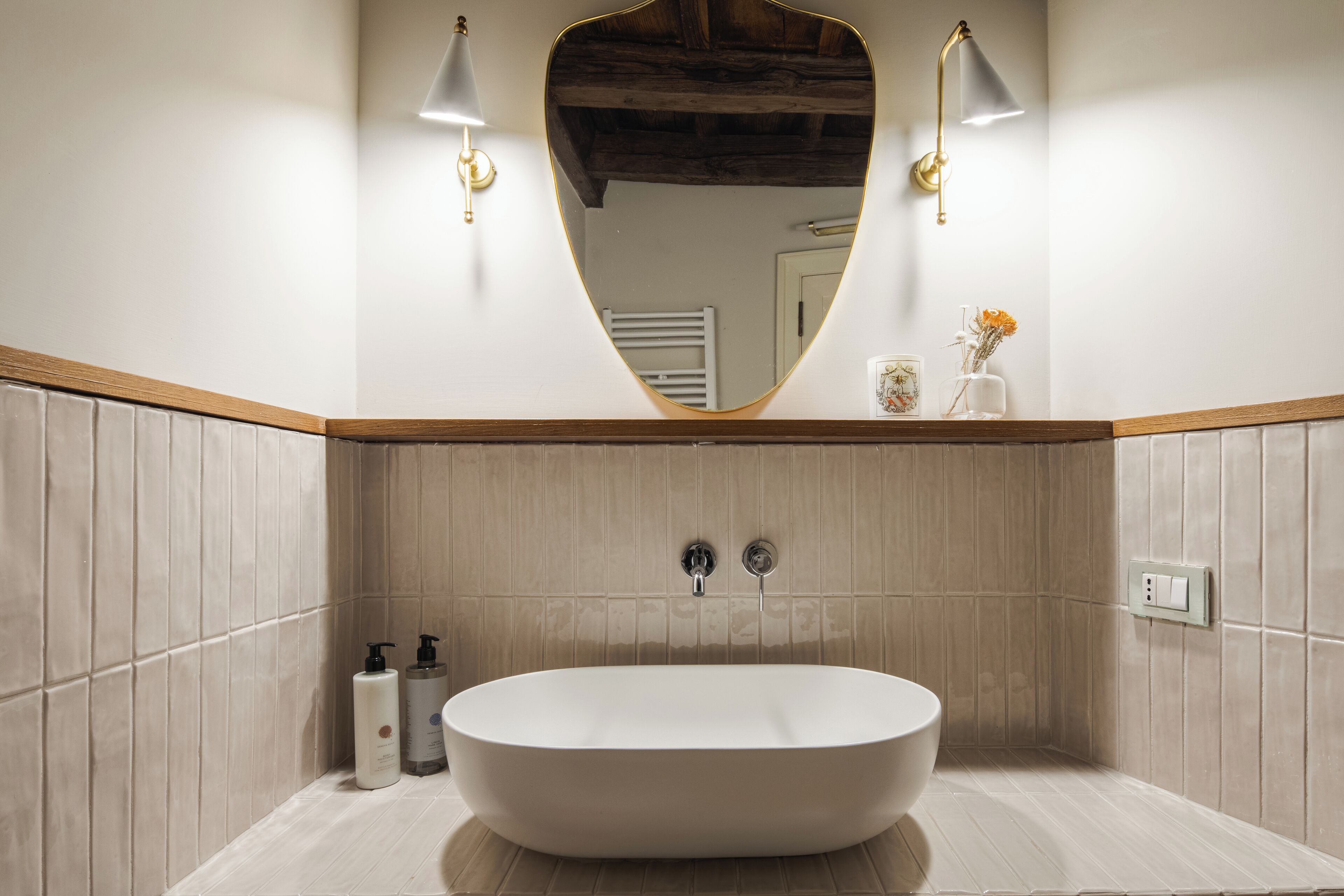A modern bathroom with a freestanding bathtub, two wall-mounted lights, and a mirror above the tub.