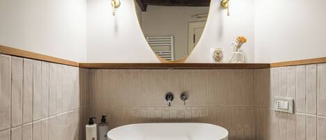 A modern bathroom with a freestanding bathtub, two wall-mounted lights, and a mirror above the tub.