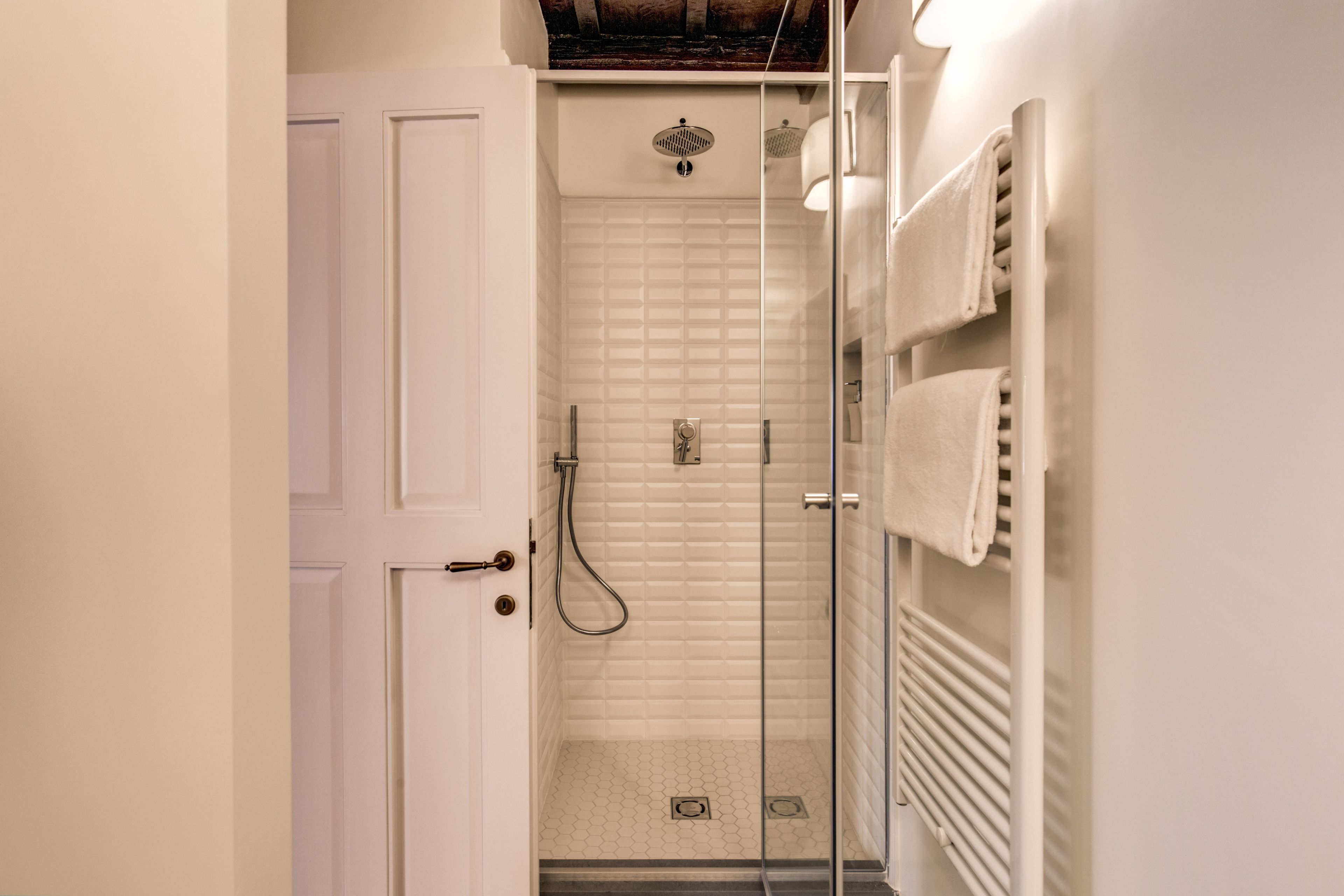 A bathroom with a glass shower enclosure, a white tiled shower wall, a towel rack, and a door.