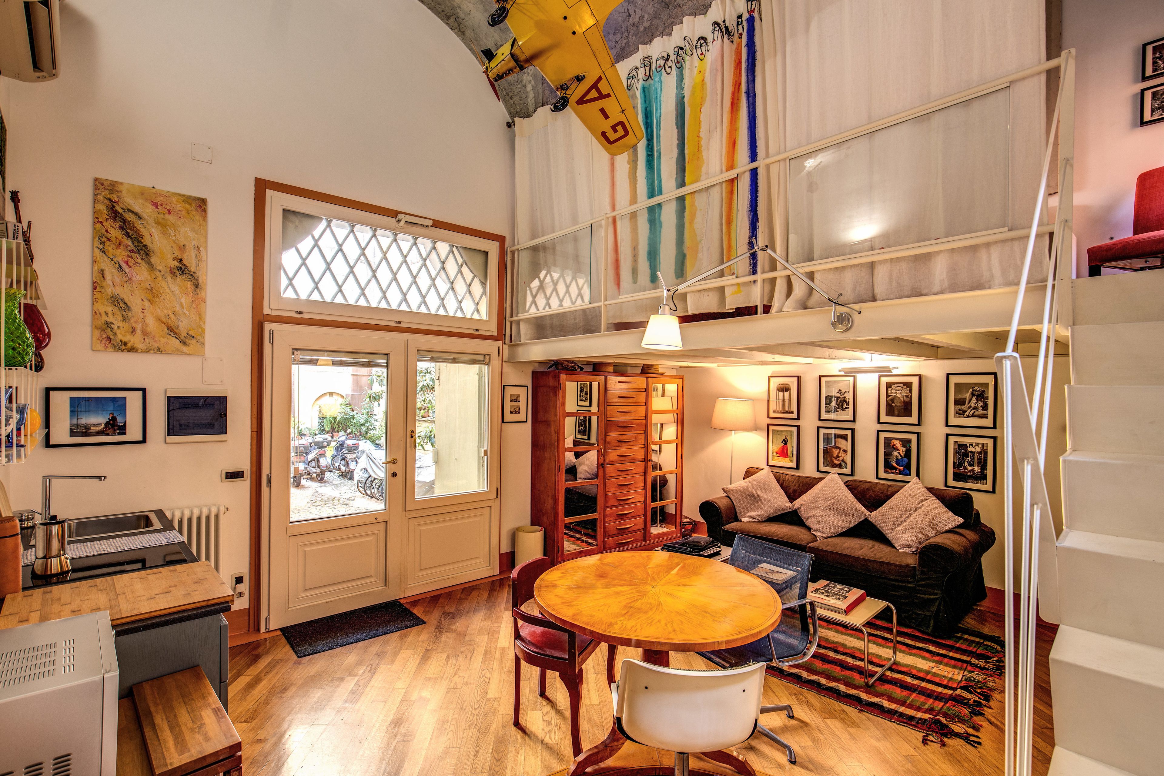 A spacious living area with a wooden dining table, a sofa, and a staircase leading to an upper level.