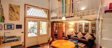 A spacious living area with a wooden dining table, a sofa, and a staircase leading to an upper level.