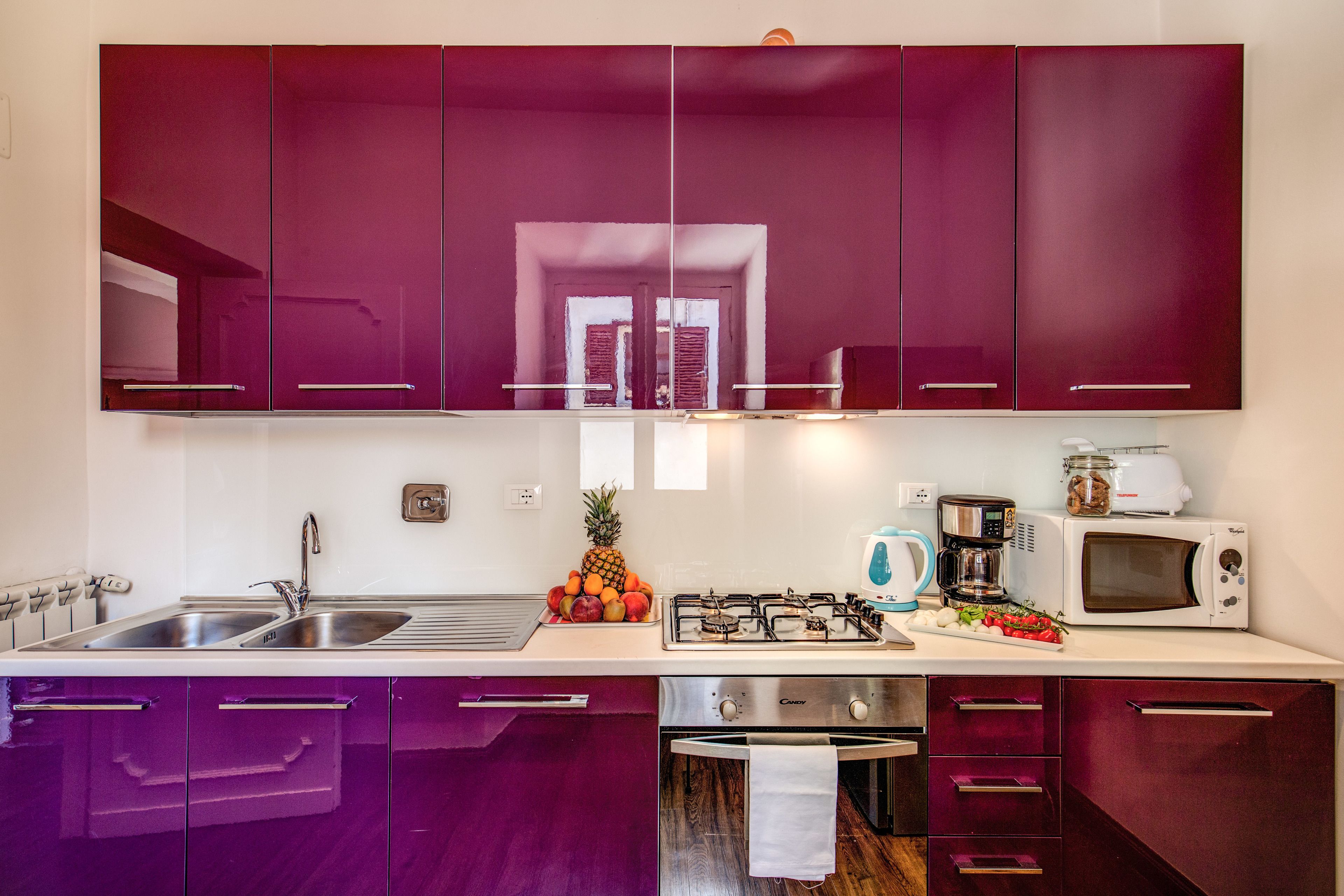 A kitchen with purple cabinets, a stainless steel sink, a gas stove, a microwave, and a toaster.