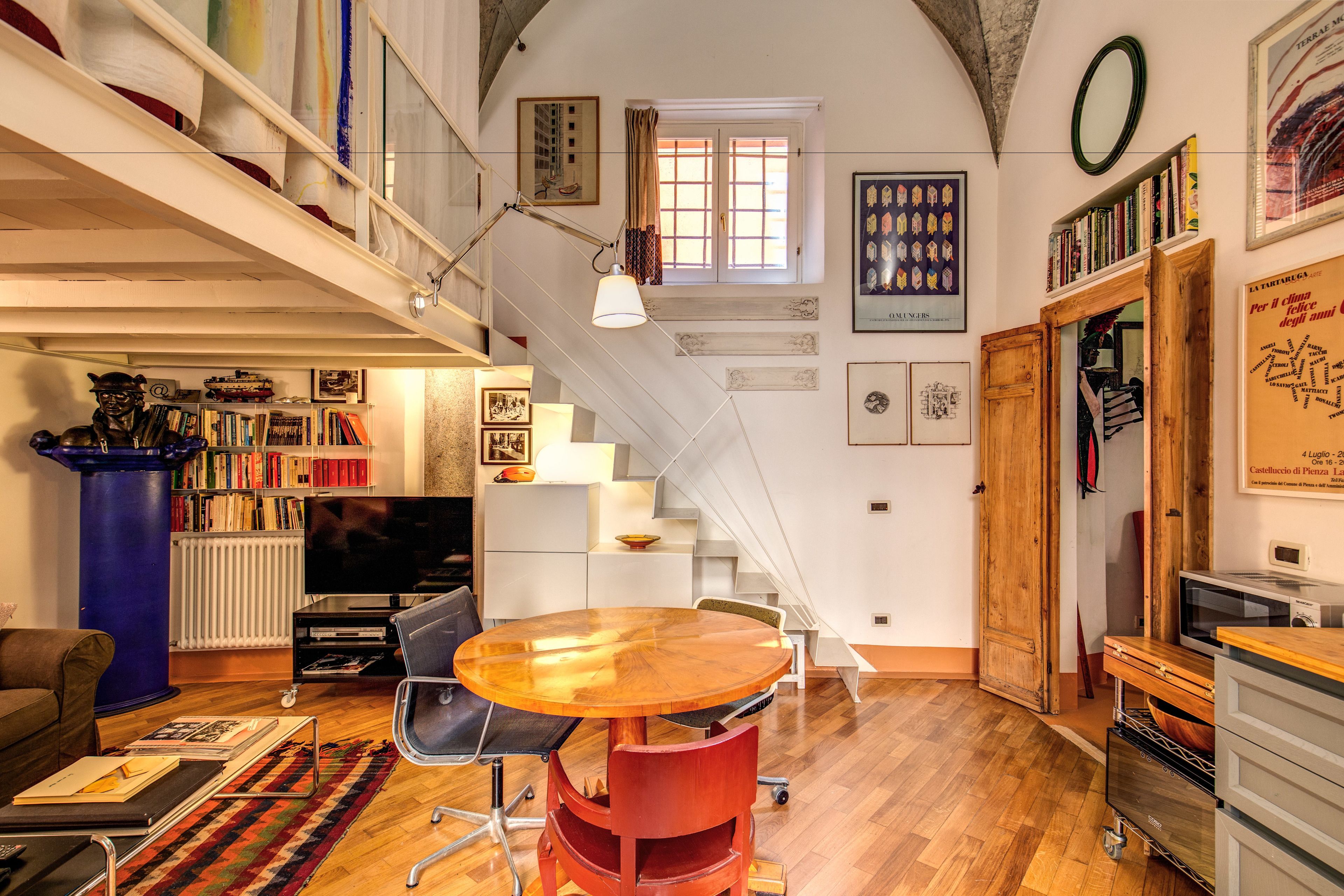 A spacious living area with a wooden dining table, a staircase, and a bookshelf filled with books.