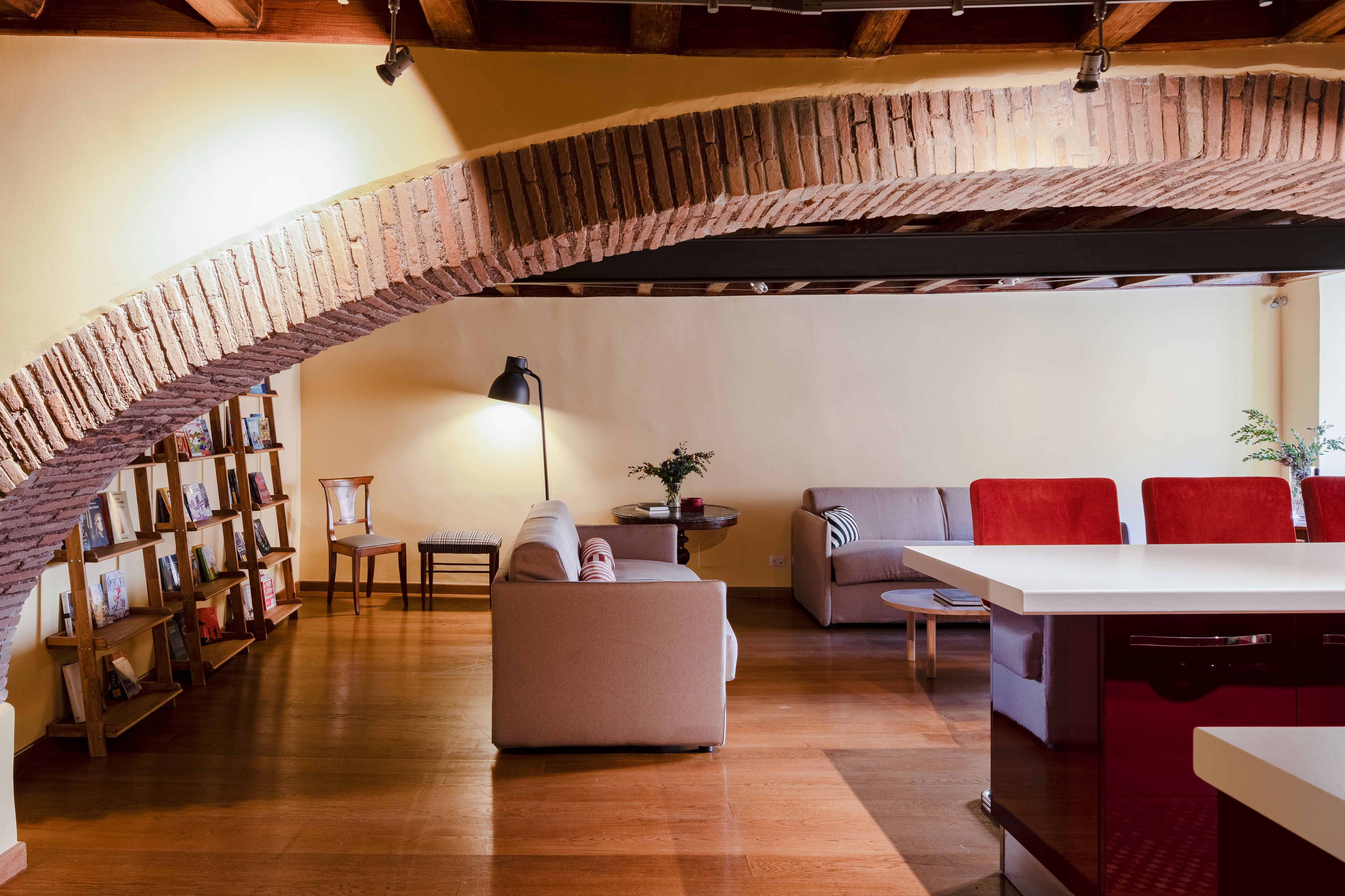A spacious living area with a brick arch, a sofa, a dining table, and a bookshelf.