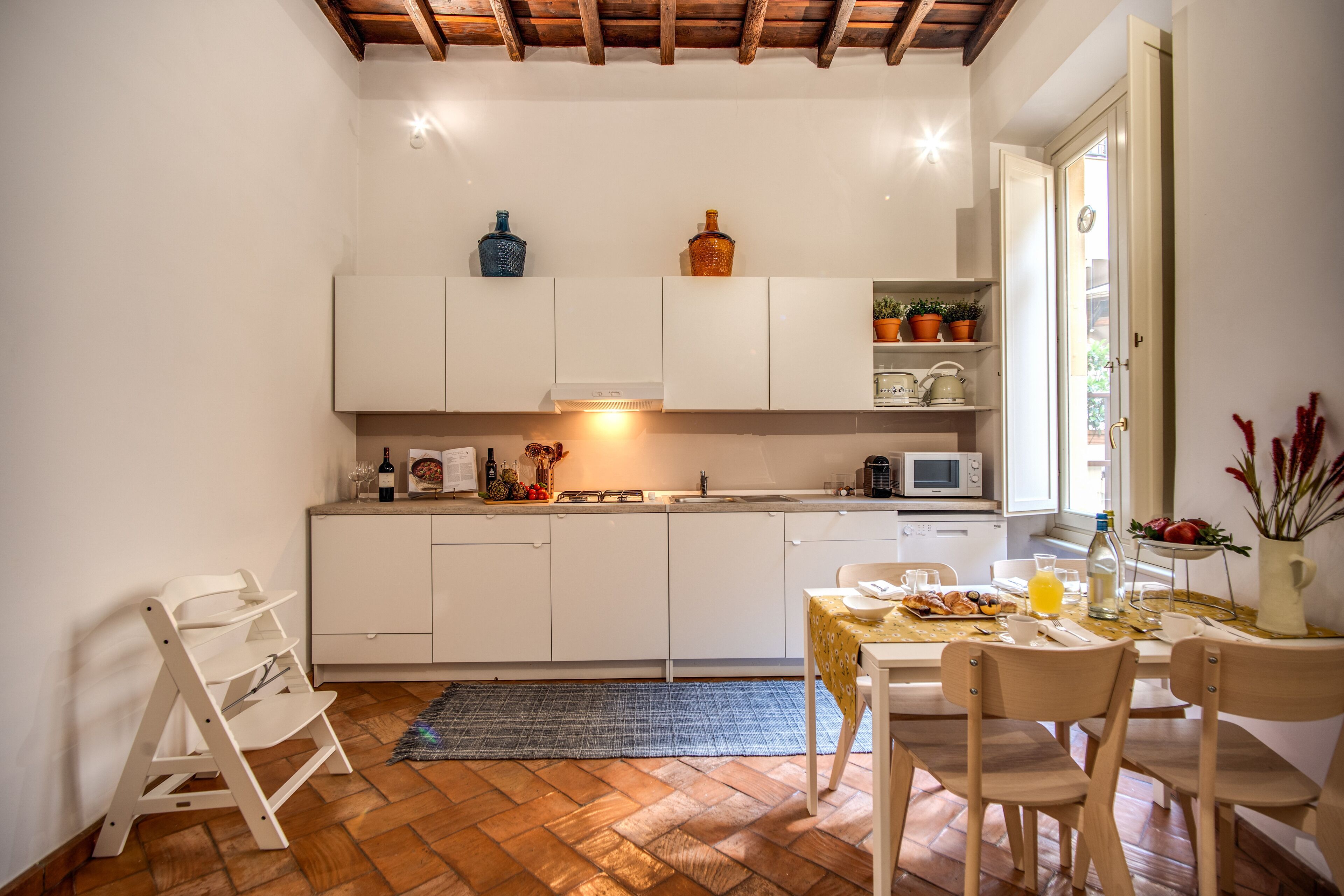 A compact kitchen with white cabinets, a wooden ceiling, and a dining area with a table set for two.
