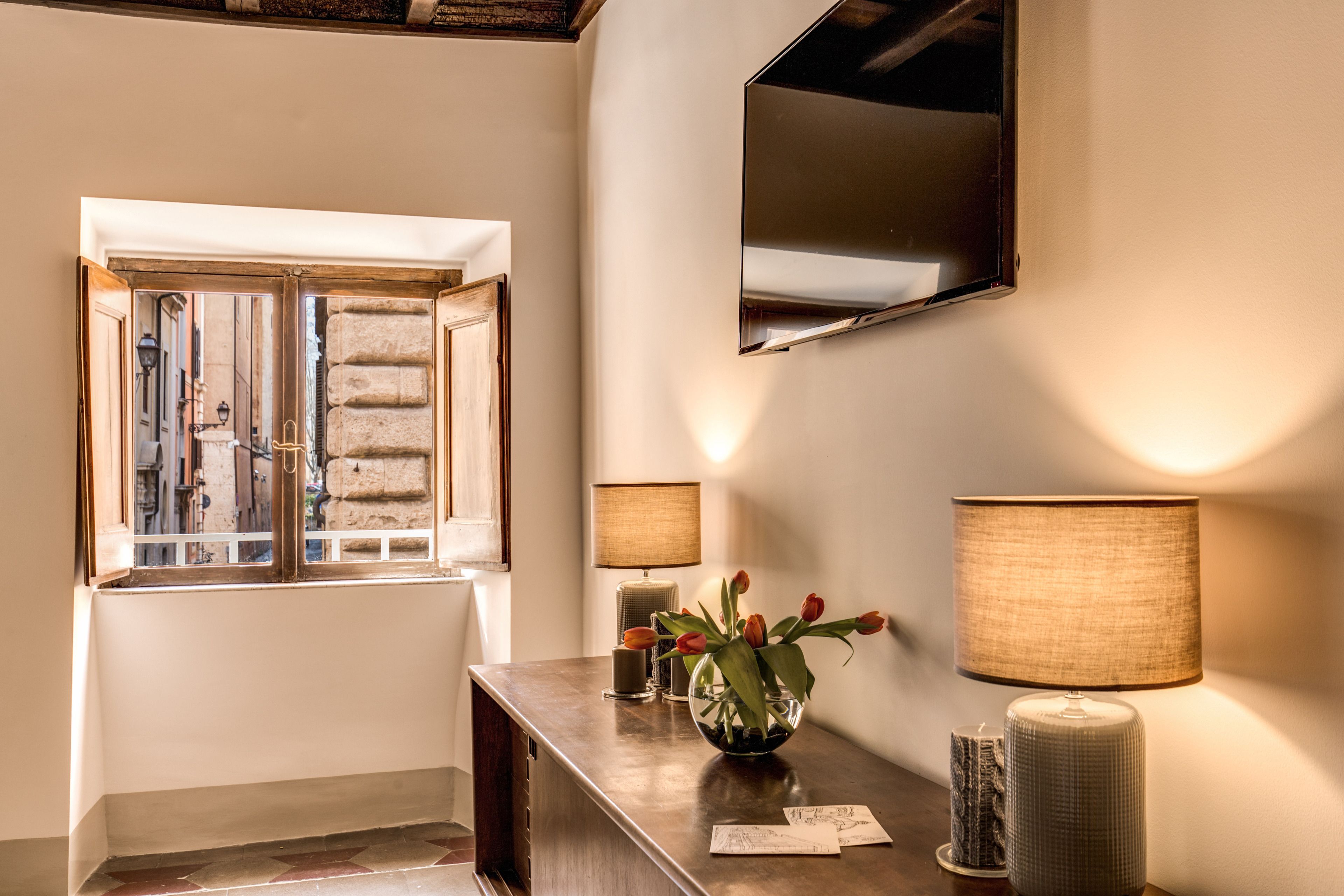 A hallway with a wooden bench, a vase with flowers, a lamp, and a mirror on the wall.