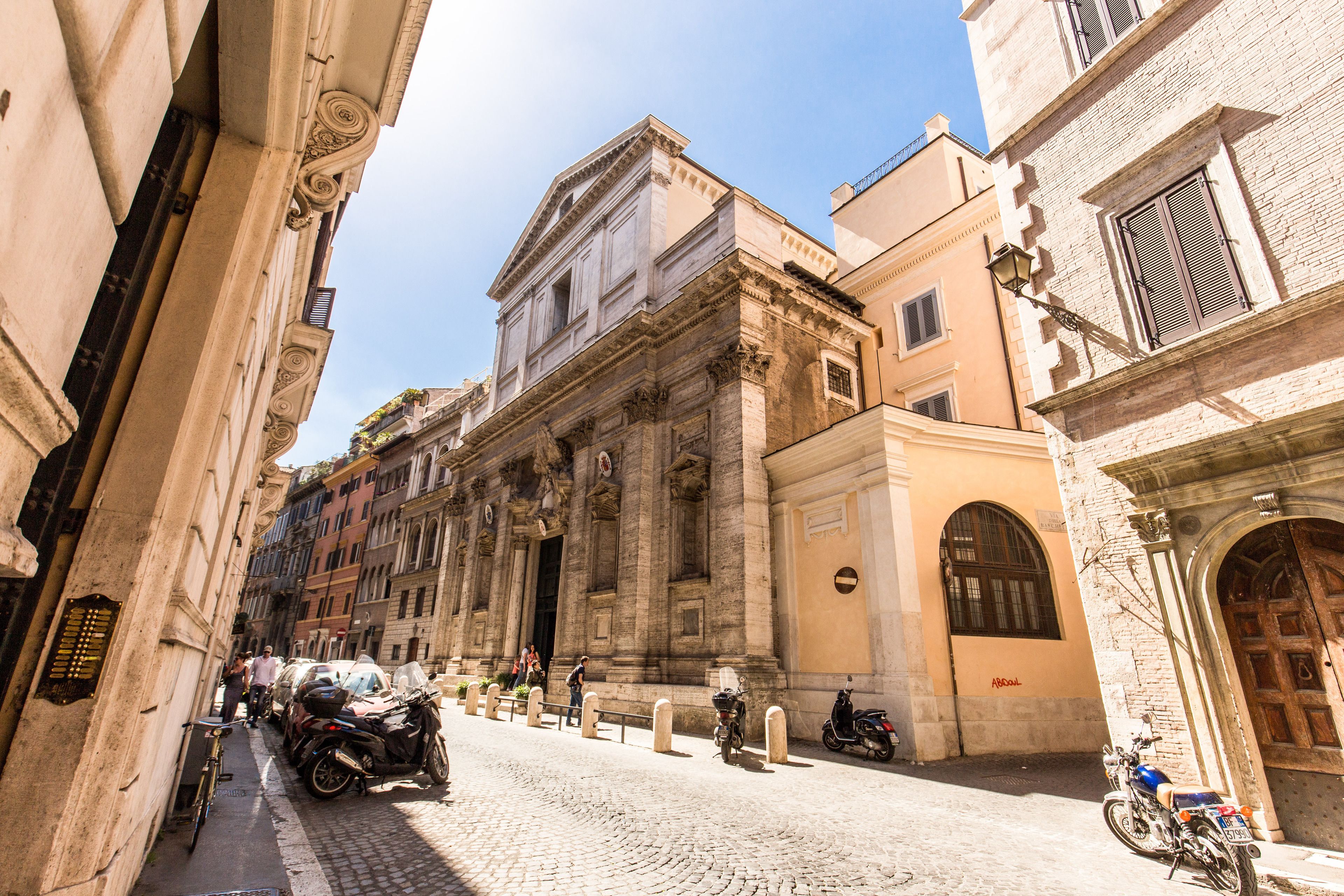 A cobblestone street with historic buildings, parked motorcycles, and bicycles.