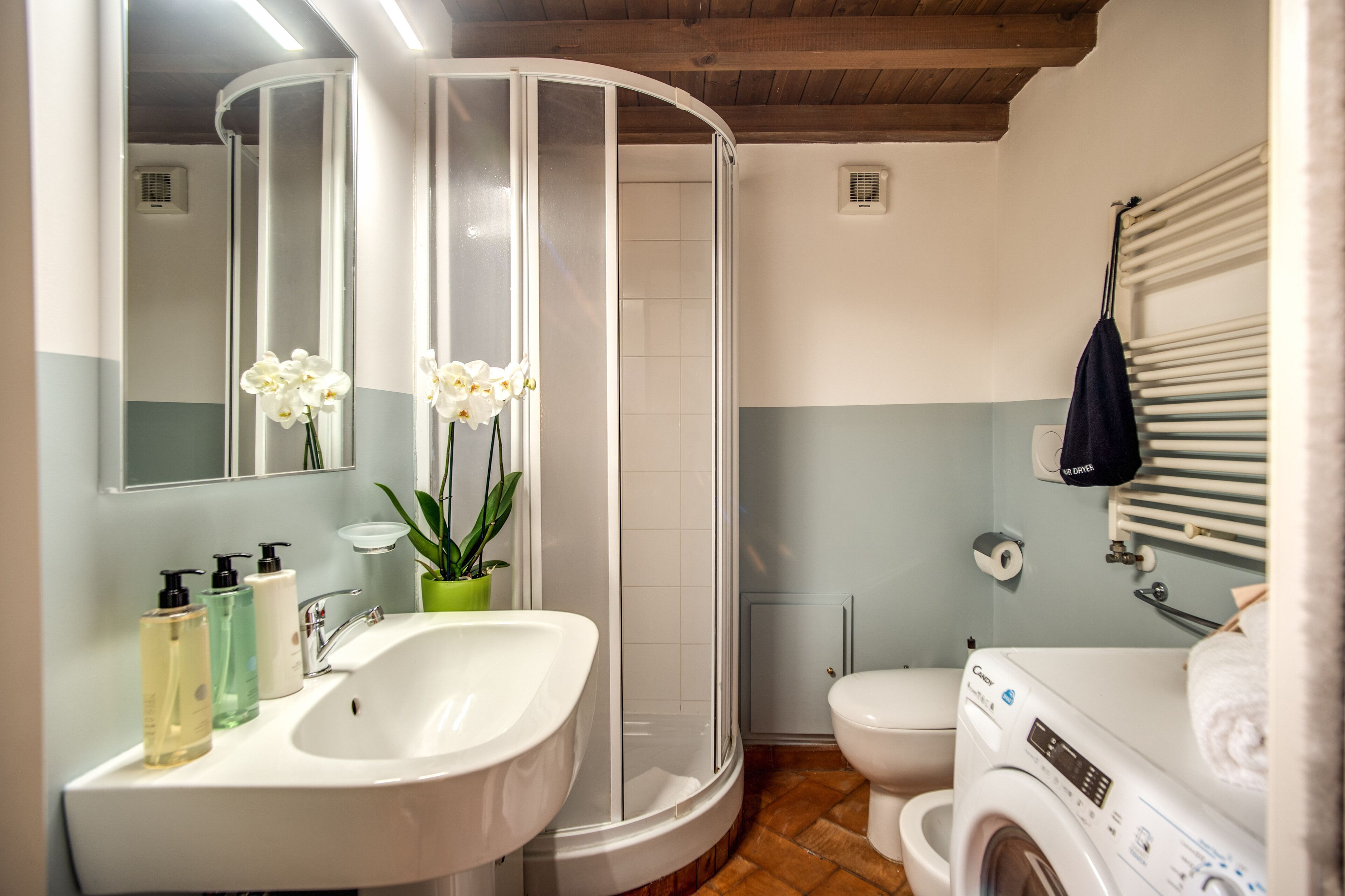 Un baño con lavamanos blanco, espejo, ducha, inodoro y lavadora.
