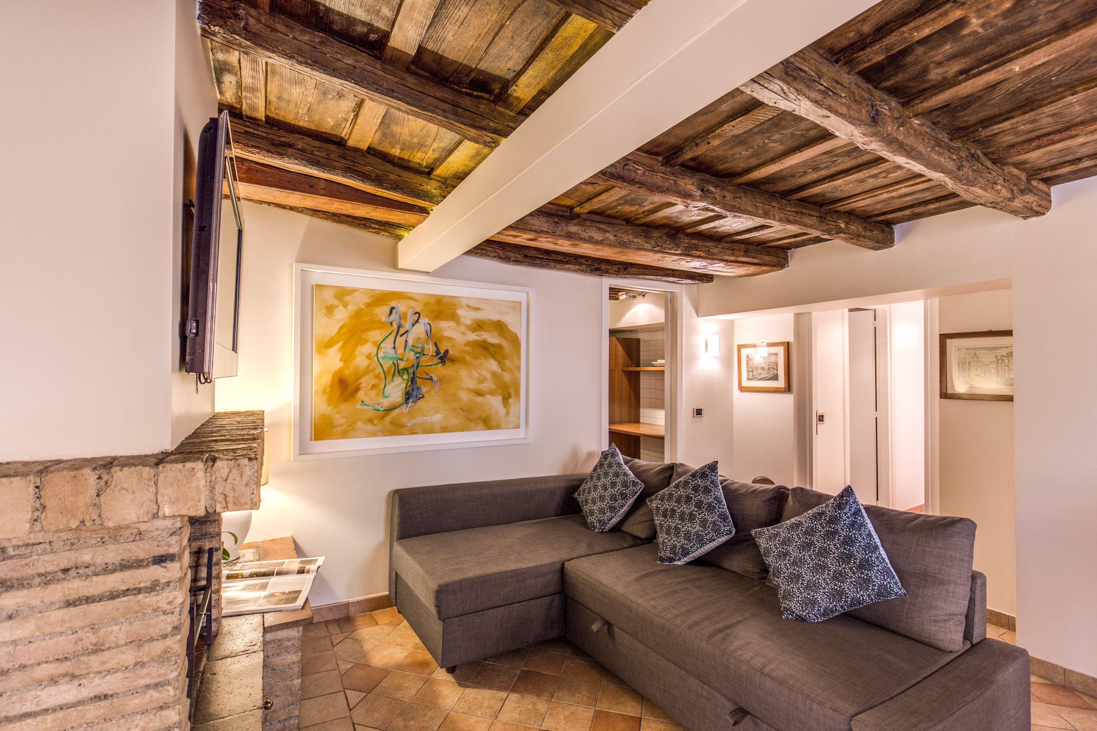 Una sala de estar acogedora con chimenea de piedra, un sofá seccional gris con cojines estampados y techo de madera.
