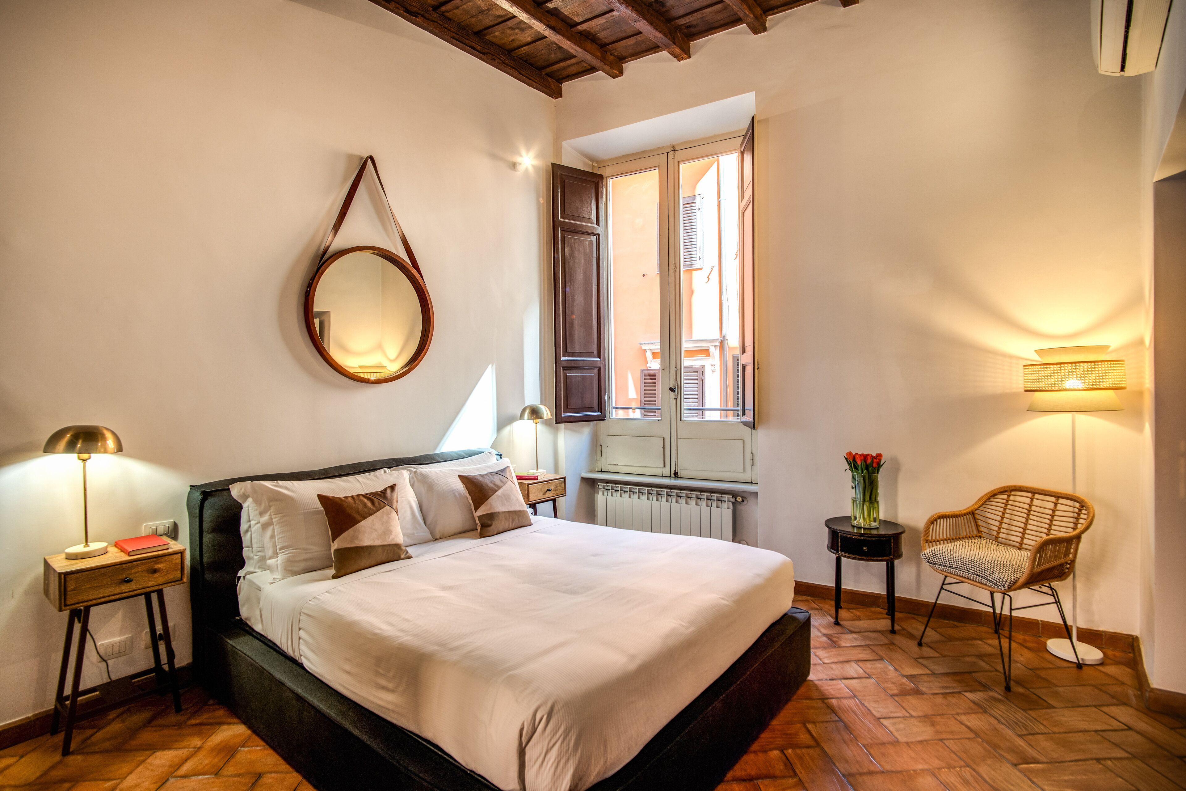 A bedroom with a bed, bedside tables, a mirror, a chair, and a window with shutters.