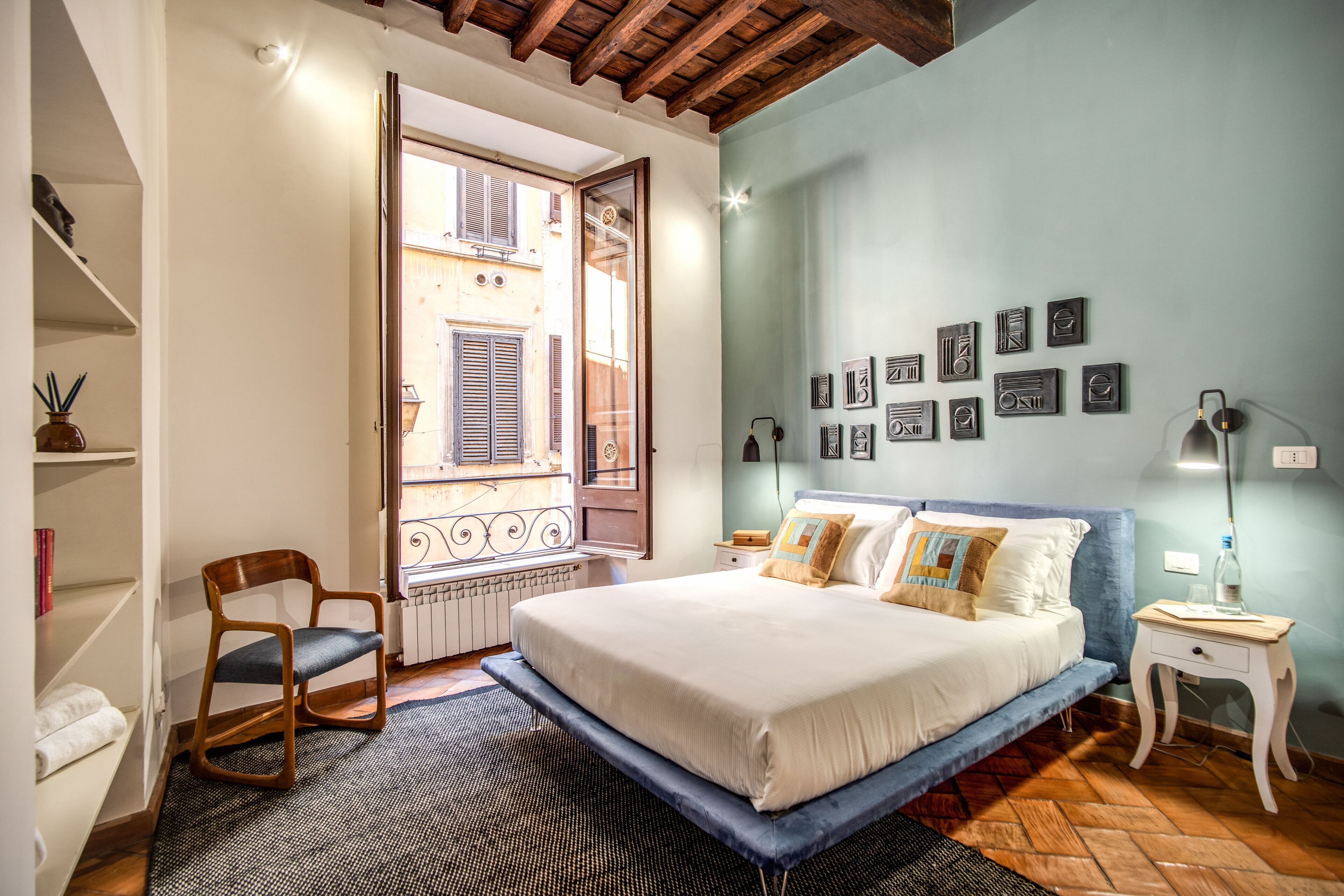 A bedroom with a bed, a chair, a nightstand, and a wall with framed pictures.
