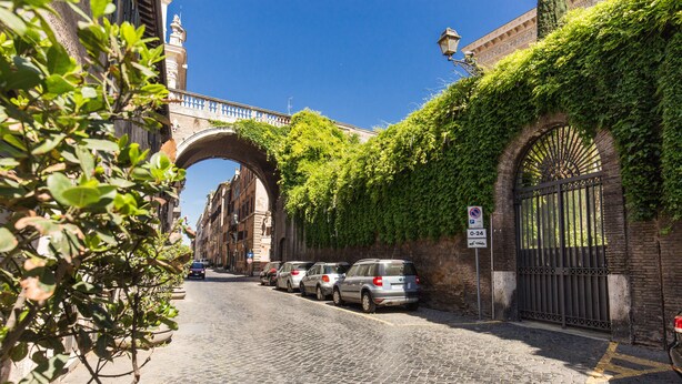 A cobblestone street with parked cars and a bridge in the background. - Your Suite Rome (Rome)